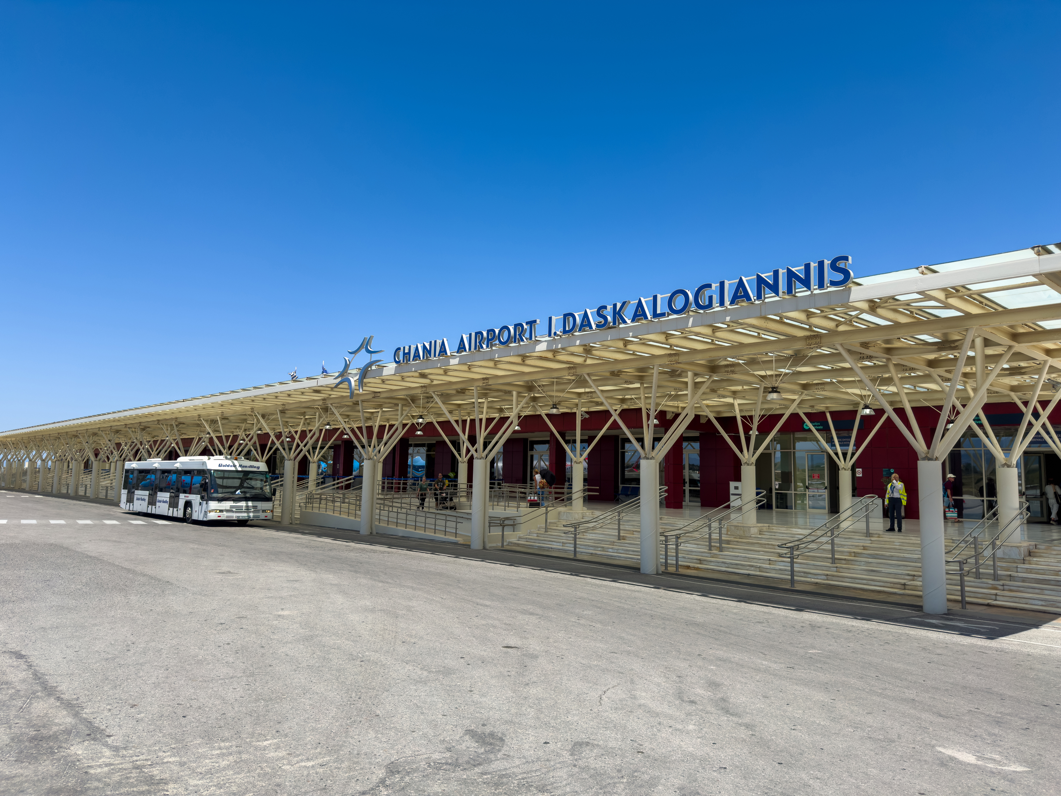 Greece. Crete island. May 20, 2025. Chania Airport I. Daskalogiannis terminal entrance with sign, buses parked under the canopy structure